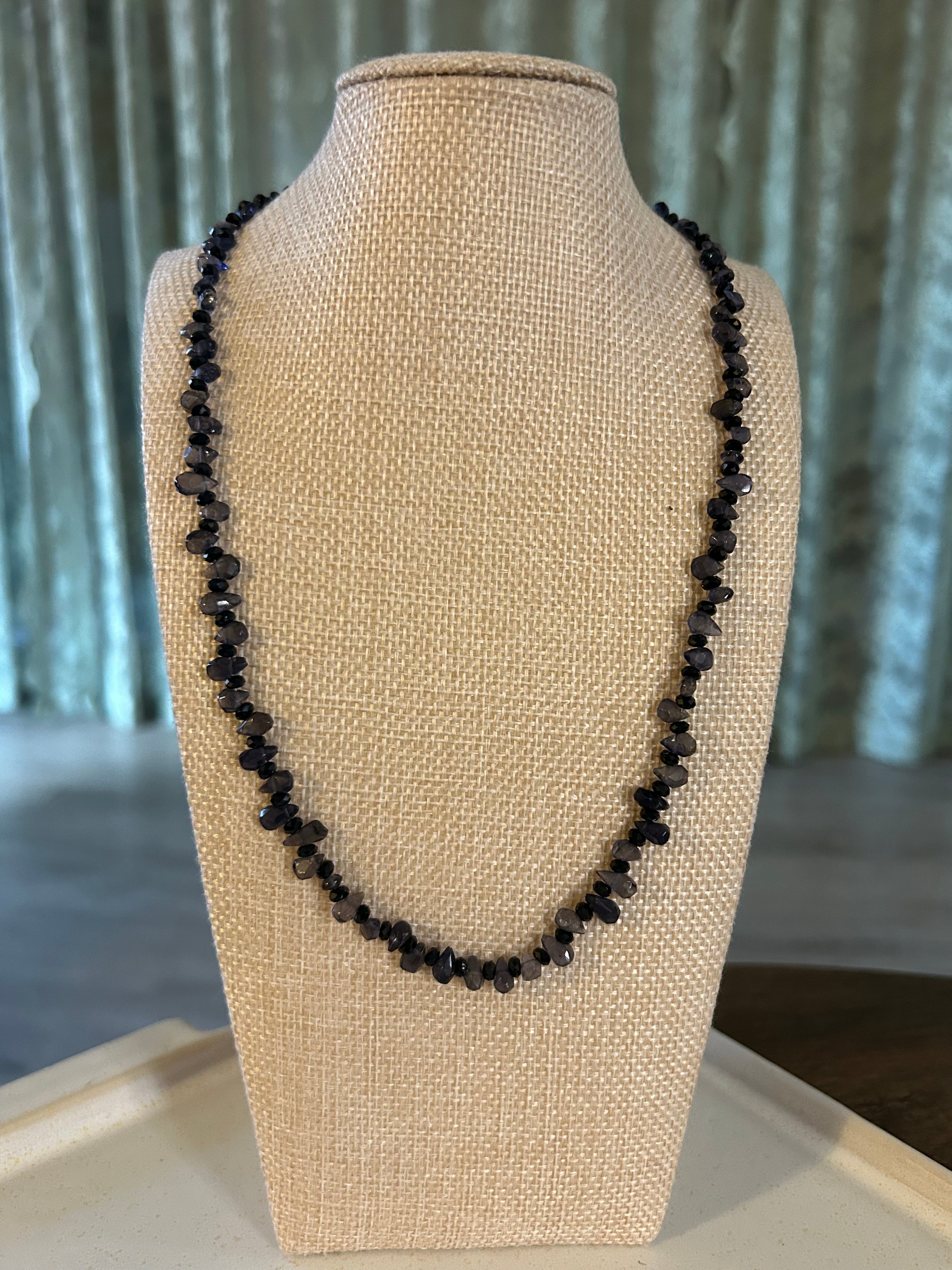 Black beaded necklace on a beige mannequin bust against a neutral background