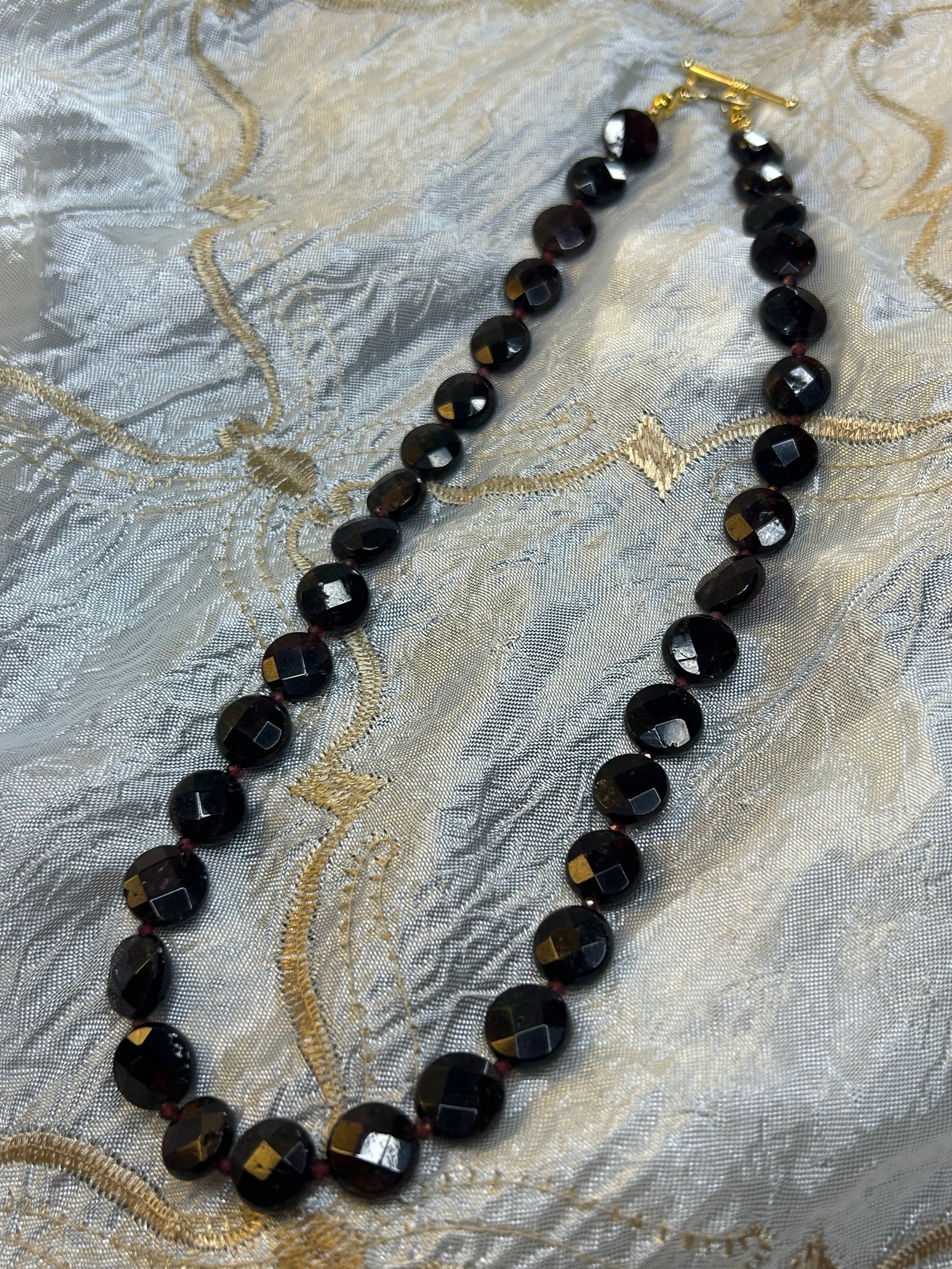 Dark red beaded necklace on a textured fabric background