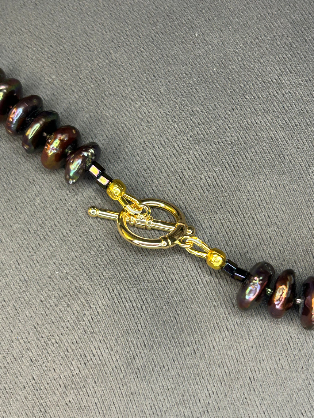 Necklace with dark pearl beads and gold clasp on a gray background