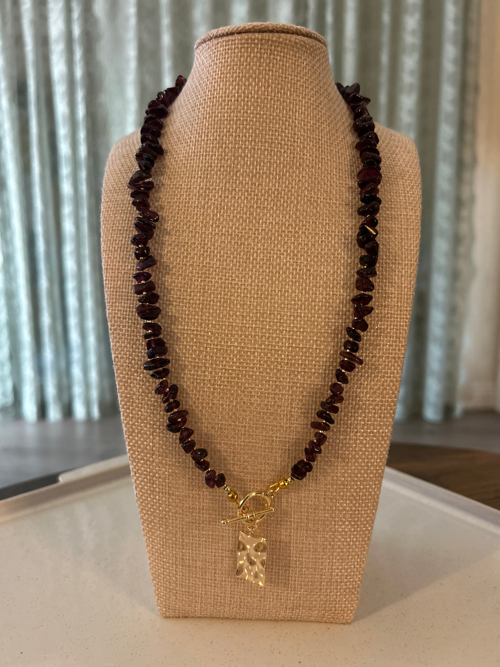 Necklace with dark beads and a gold clasp on a beige stand against a neutral background