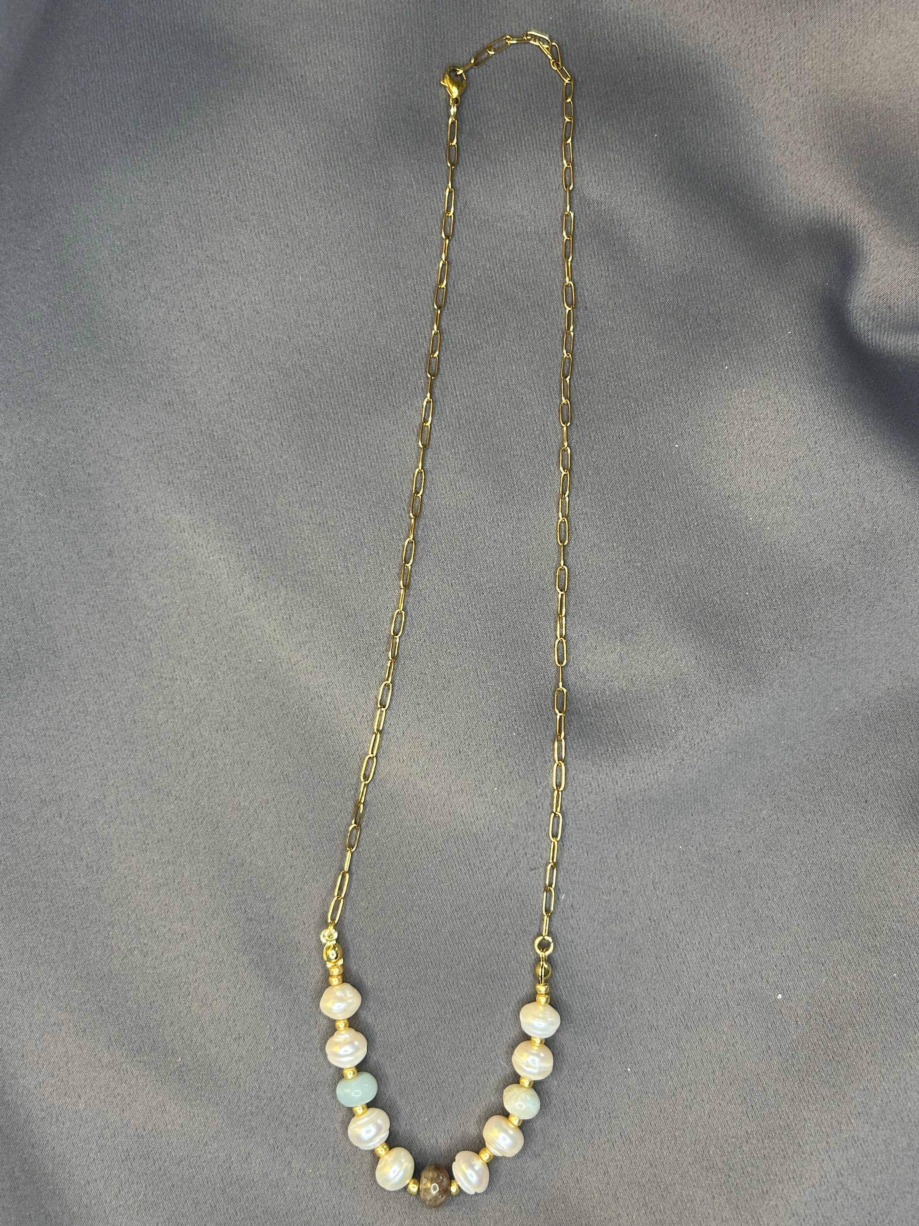 Gold chain necklace with pearls on a gray fabric background