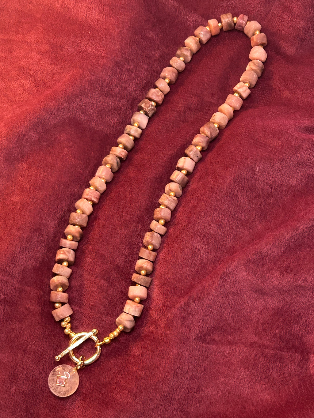 Necklace with pink beads and a gold clasp on a red fabric background