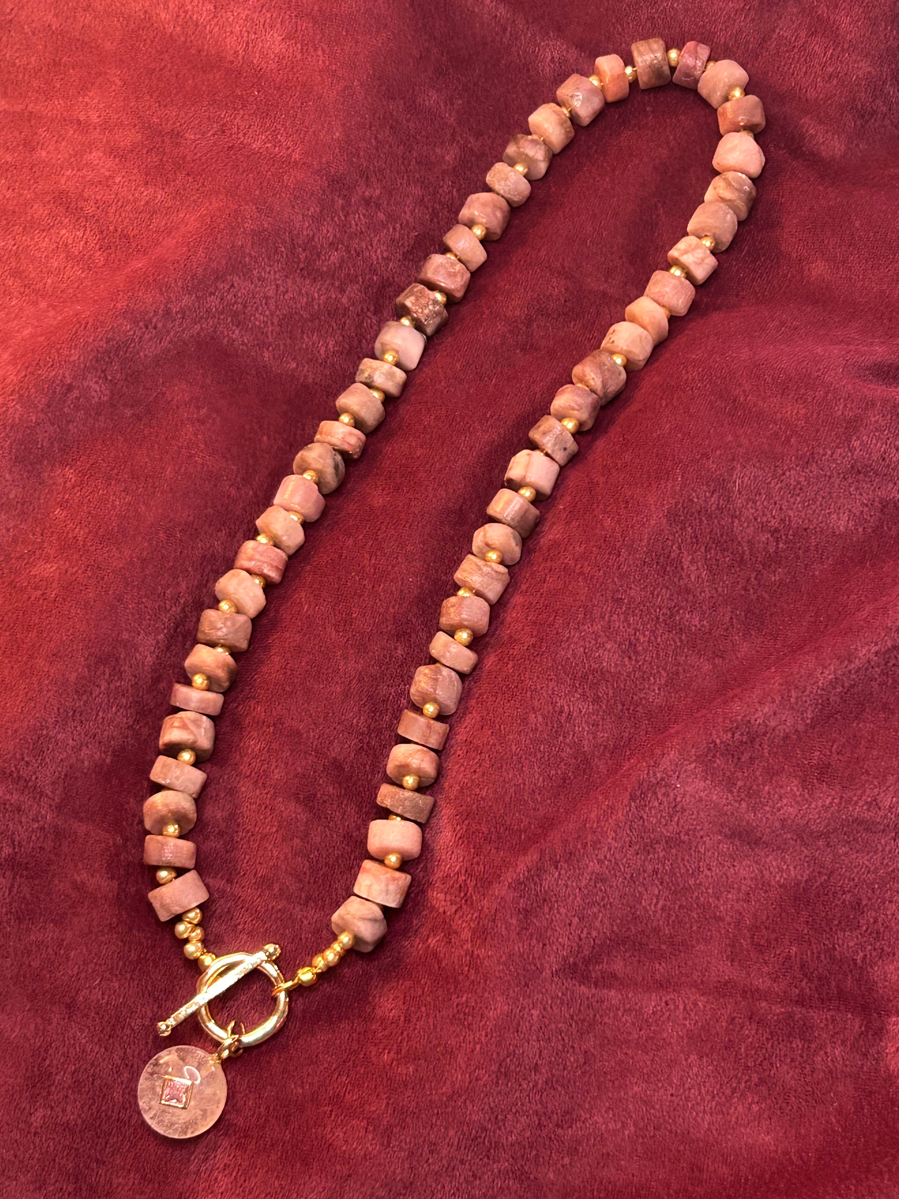 Necklace with pink beads and a gold clasp on a red fabric background