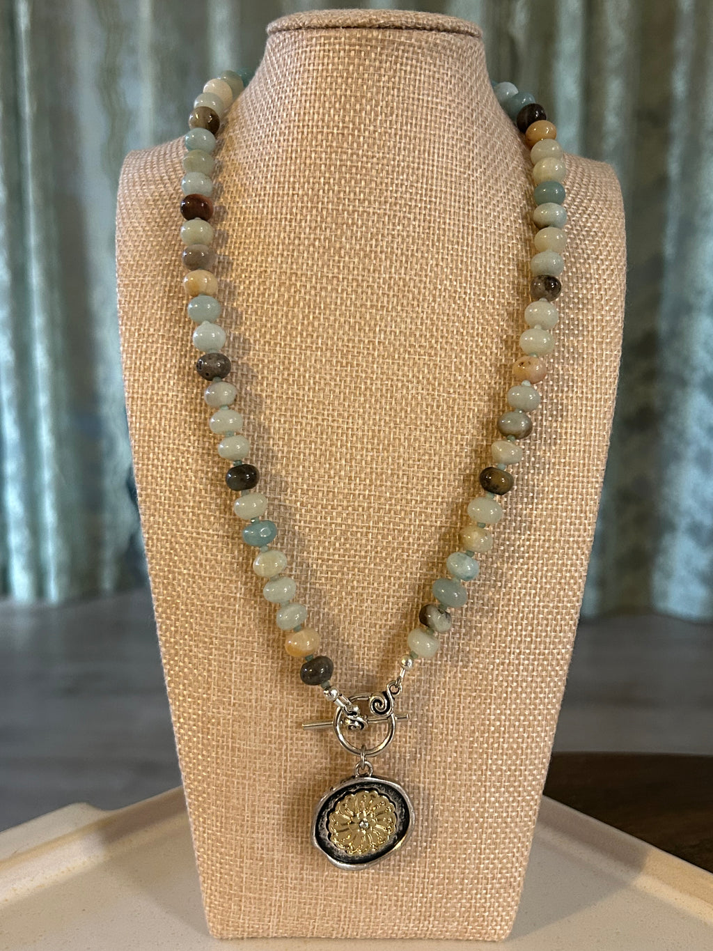 Beaded necklace with a decorative charm on a beige mannequin bust.