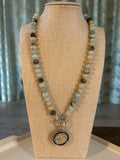 Beaded necklace with a decorative charm on a beige mannequin bust.