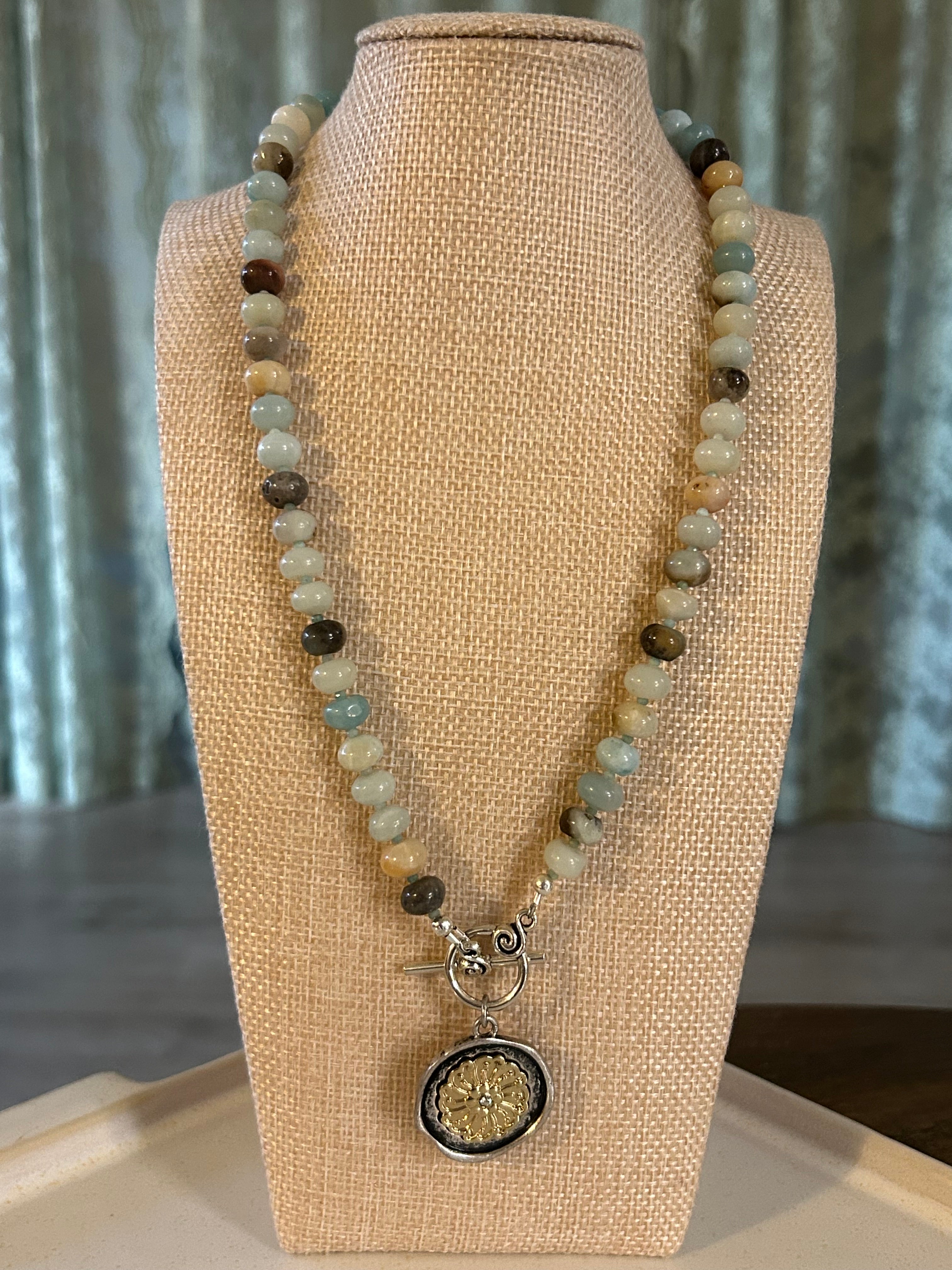 Beaded necklace with a decorative charm on a beige mannequin bust.