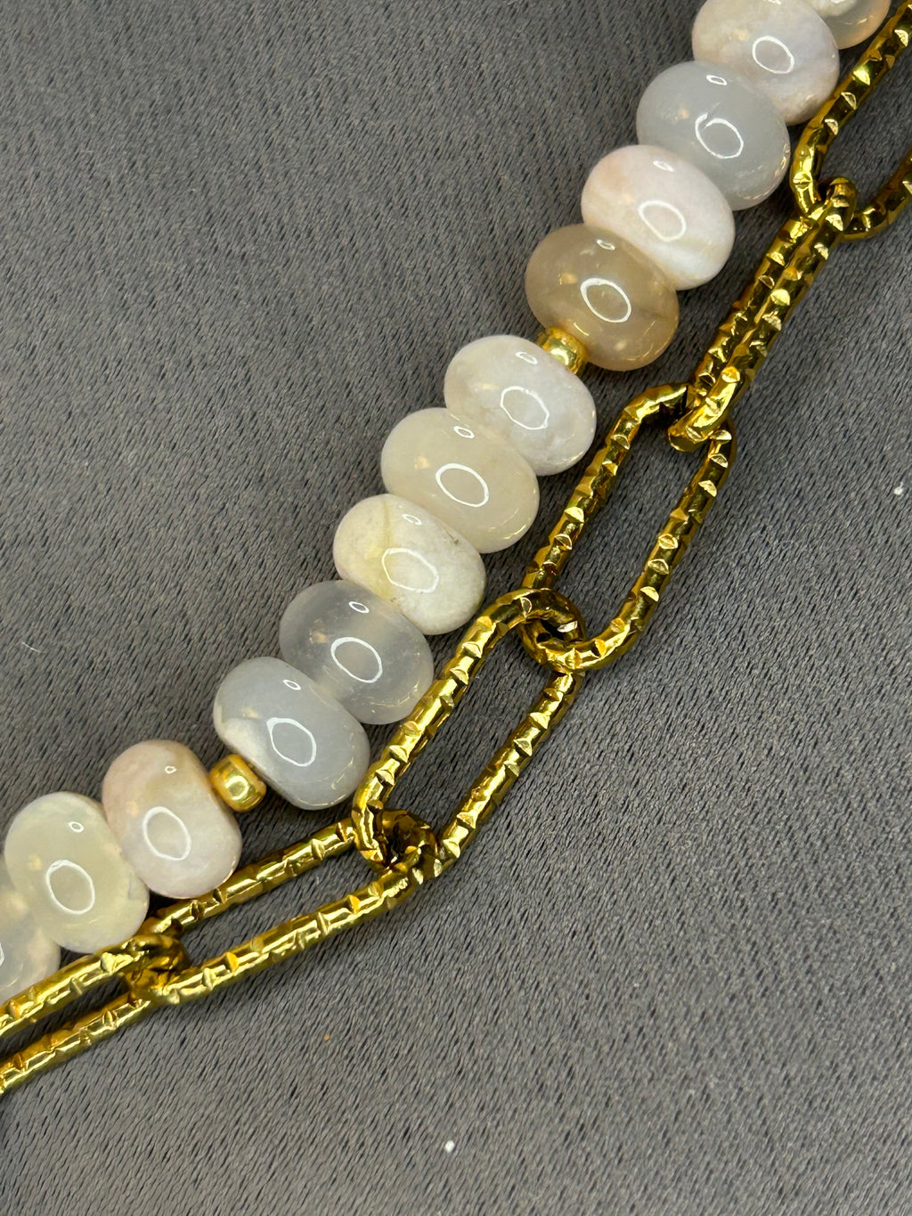 Bracelet with gold chain and light-colored beads on a gray background