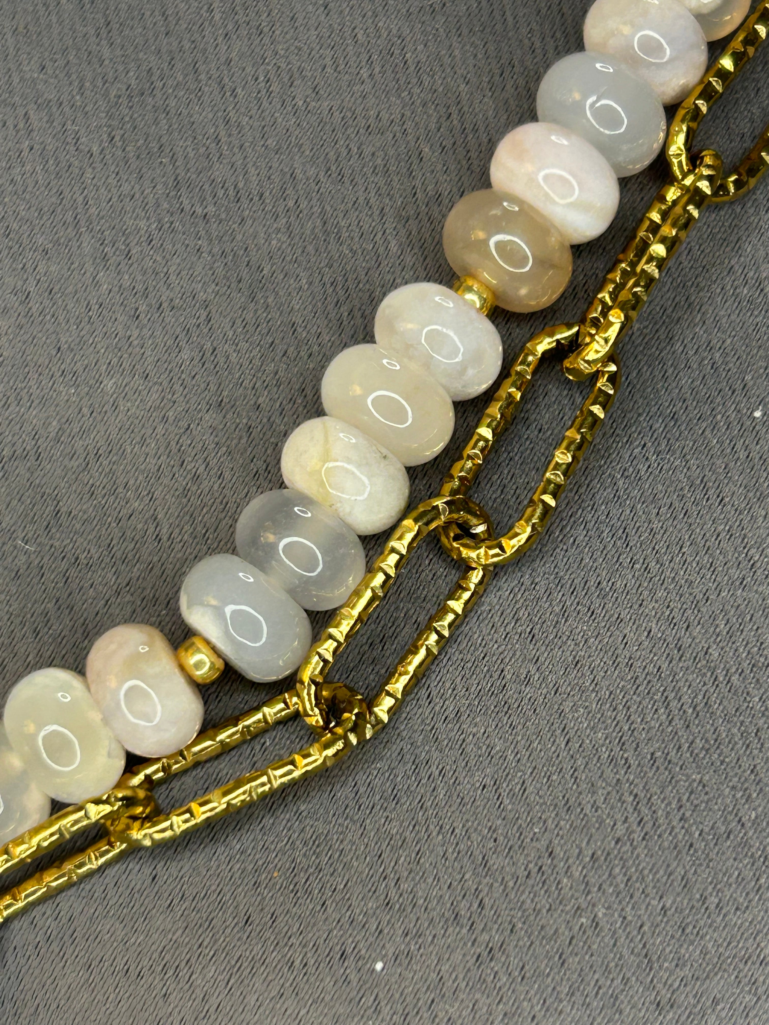Bracelet with gold chain and light-colored beads on a gray background