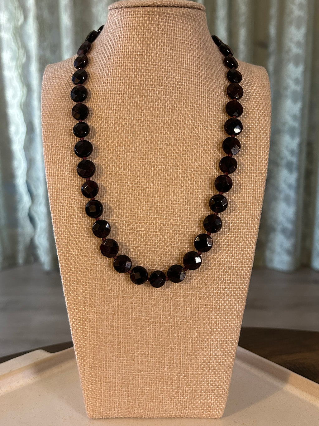 Dark red beaded necklace on a beige display against a neutral background