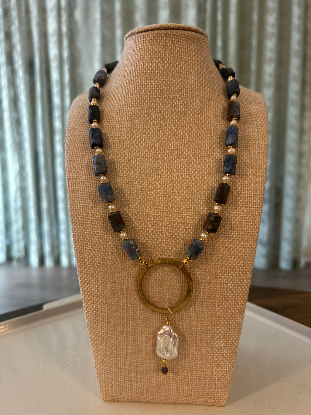 Necklace with beads and a crystal pendant on a brown jewelry display