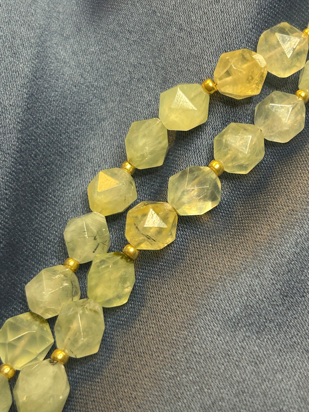 Necklace with faceted green-yellow beads on a gray fabric background