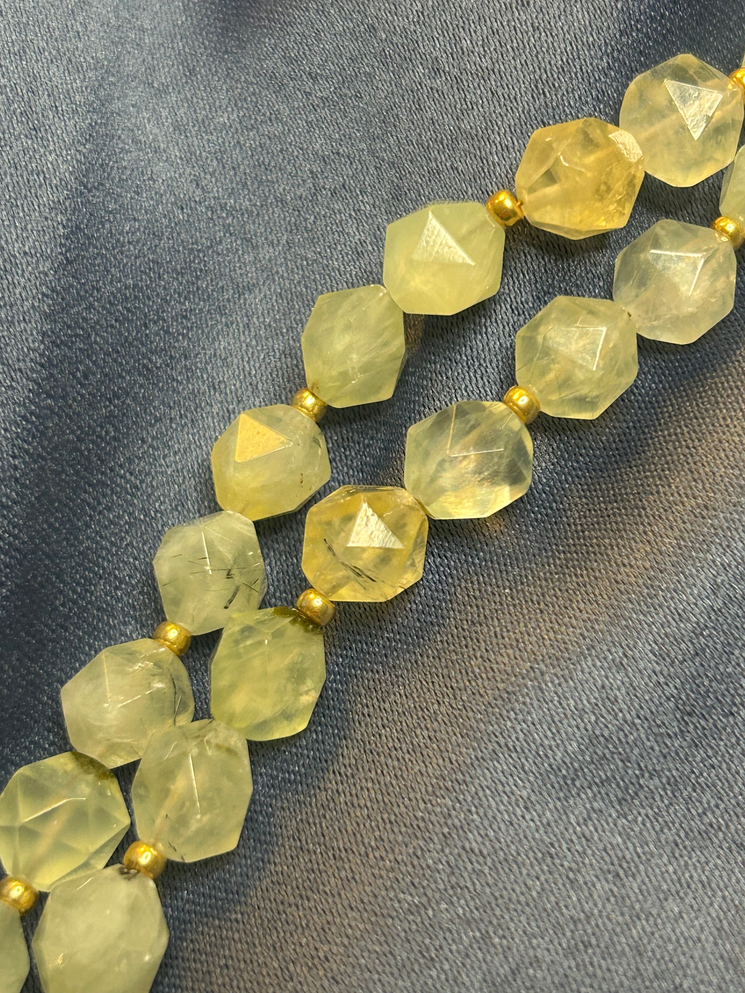 Necklace with faceted green-yellow beads on a gray fabric background