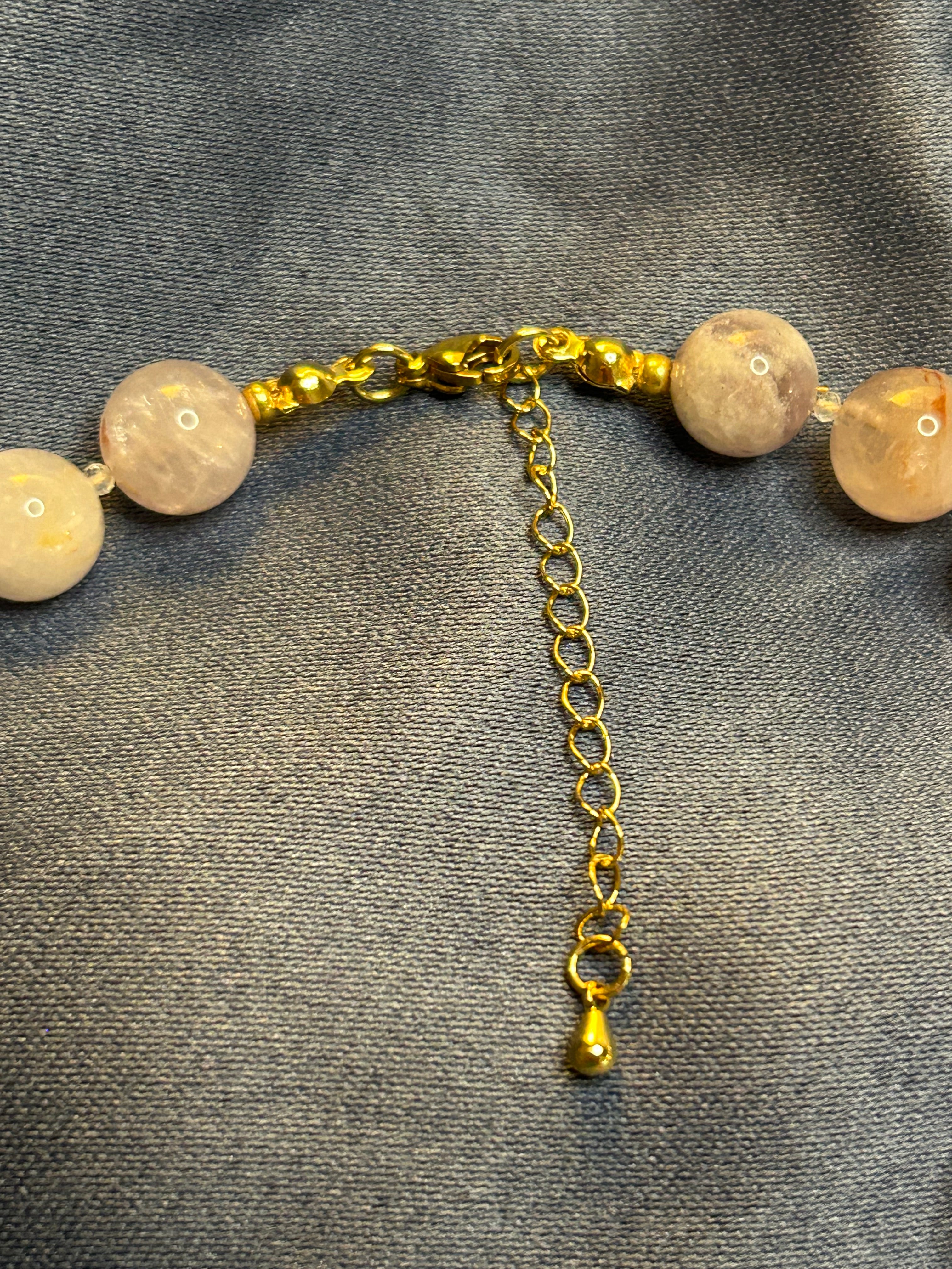 Bracelet with light-colored beads and gold chain on a gray fabric background