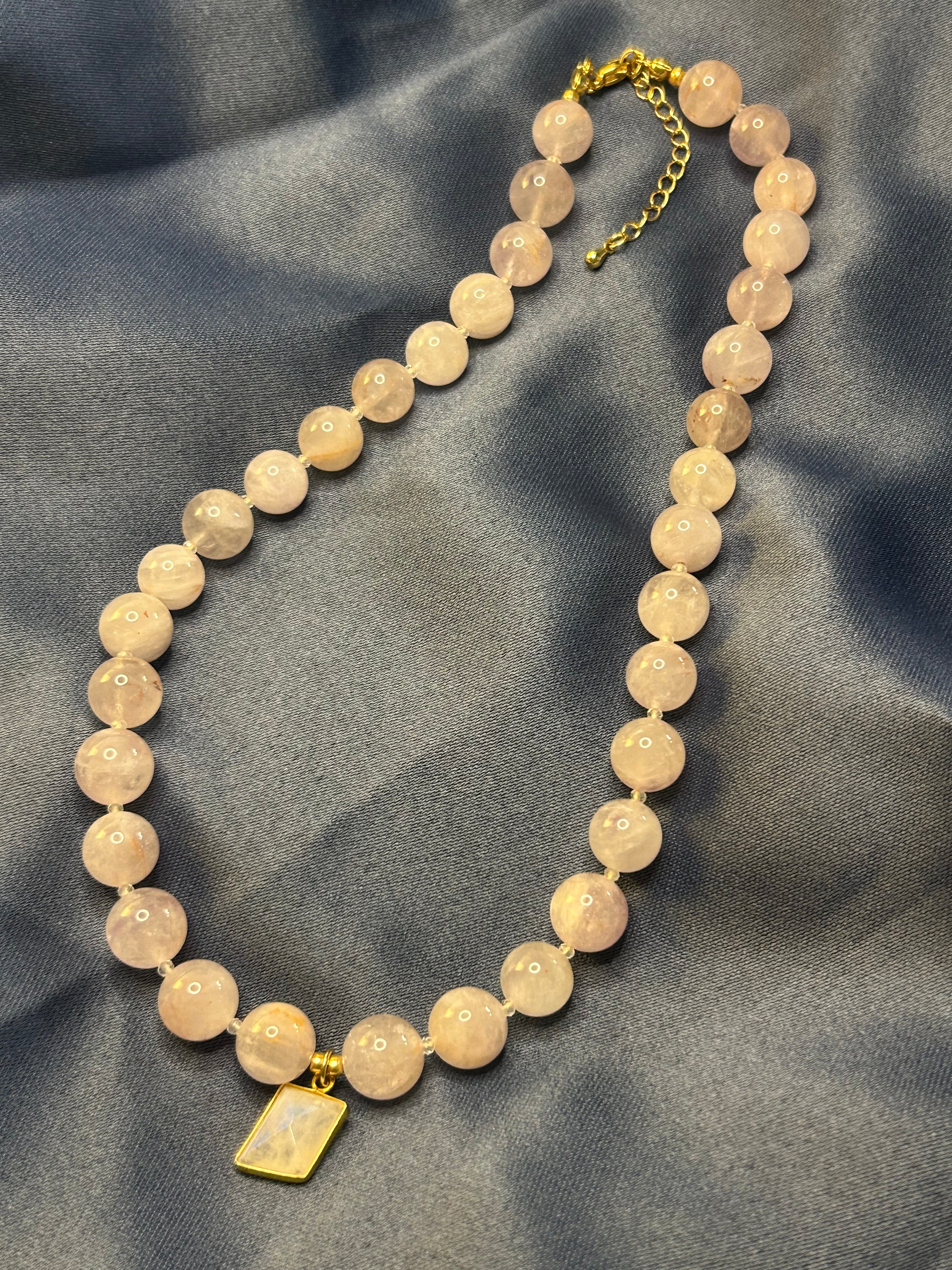 Necklace with purple beads and a gold clasp on a gray fabric background