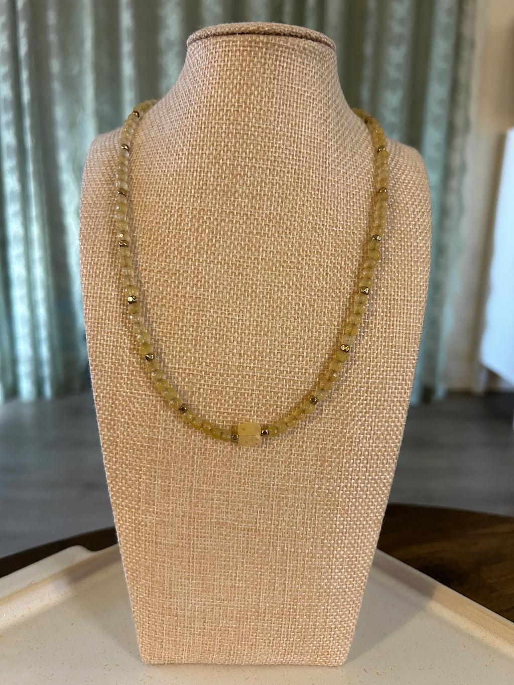 Gold beaded necklace on a mannequin bust against a neutral background