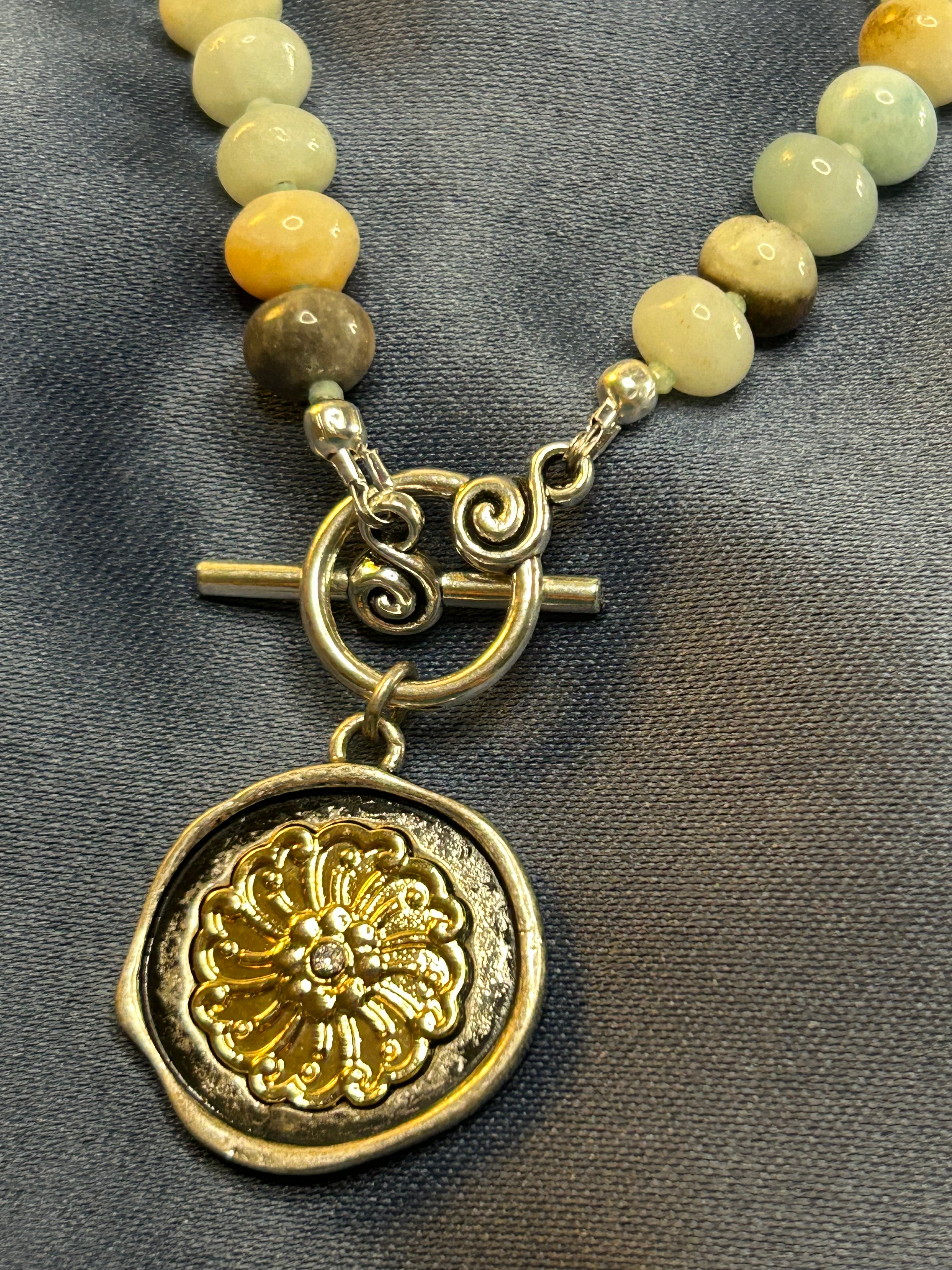 Necklace with green beads and a gold coin charm on a gray background