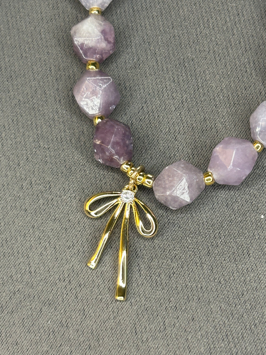 Necklace with purple beads and a gold bow clasp on a gray background