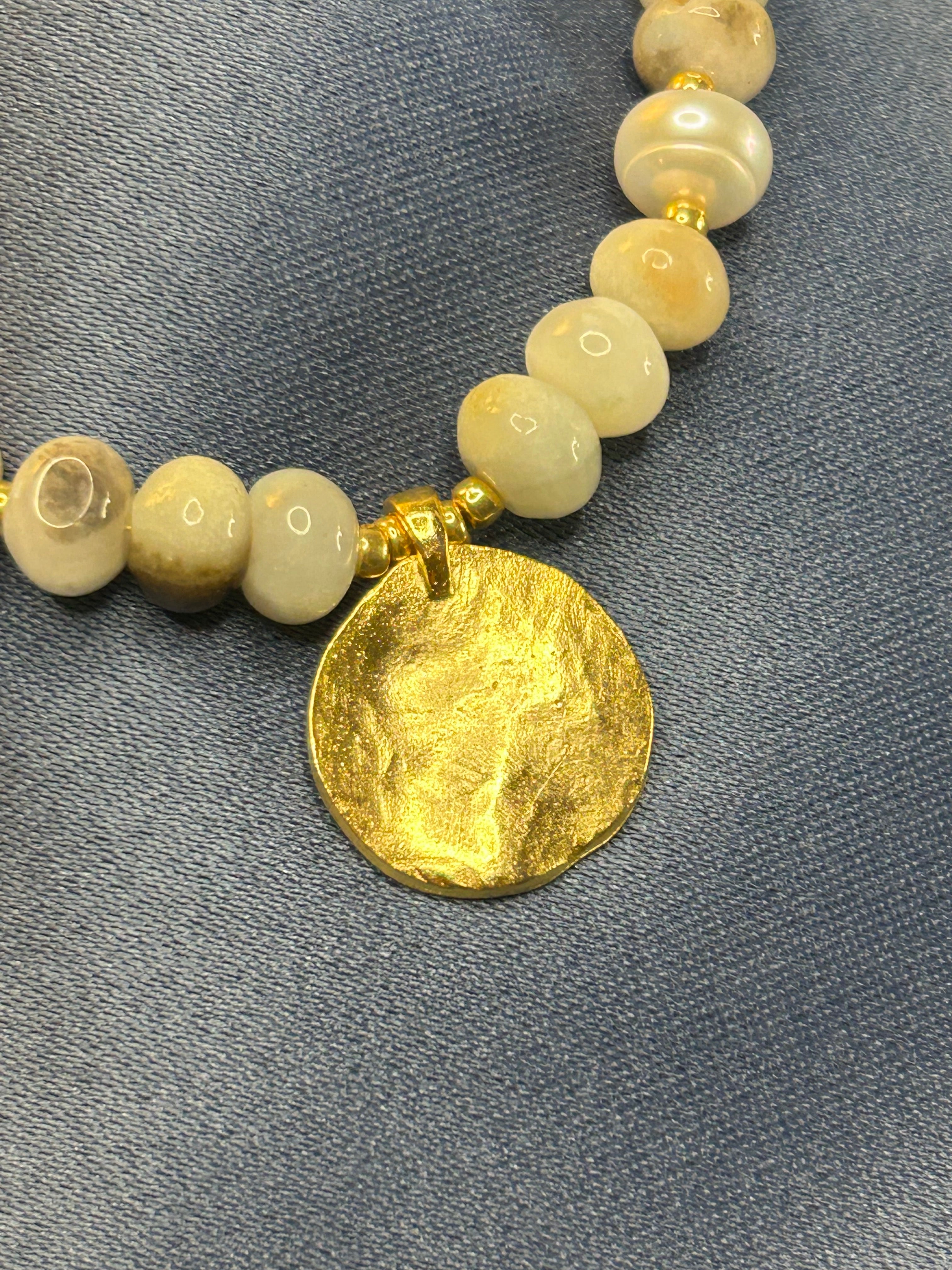 Necklace with beads and a gold disc on a gray background
