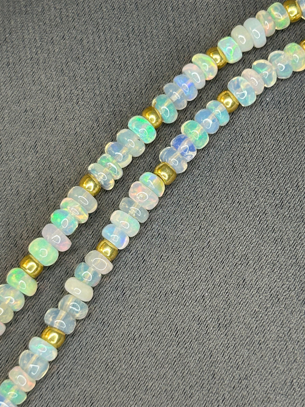 Opal beads with gold accents on a gray fabric background