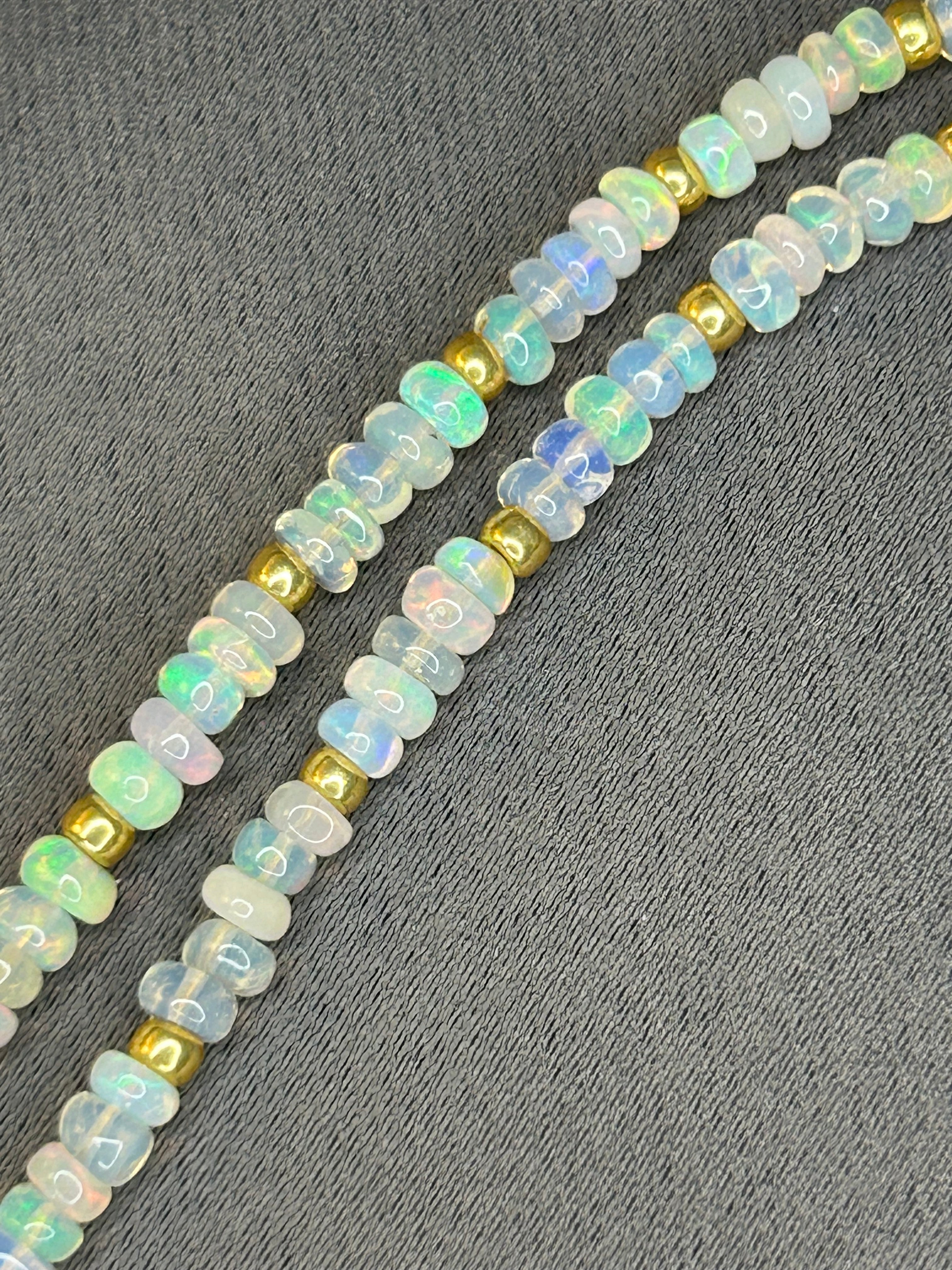 Opal beads with gold accents on a gray fabric background