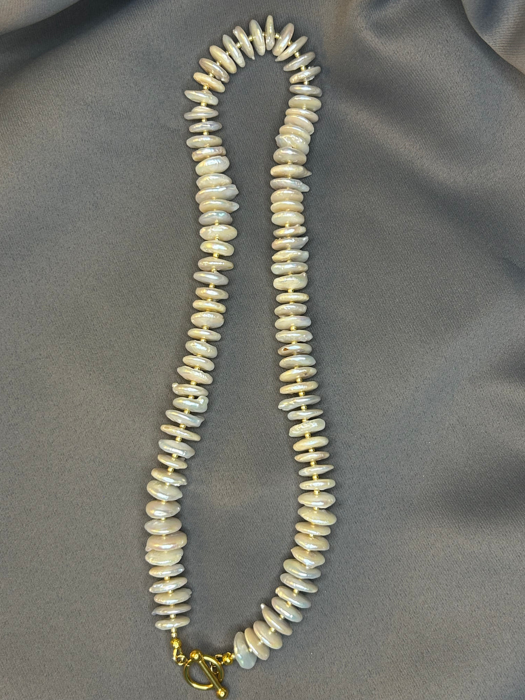 Necklace with pearl rondelle beads on a gray fabric background