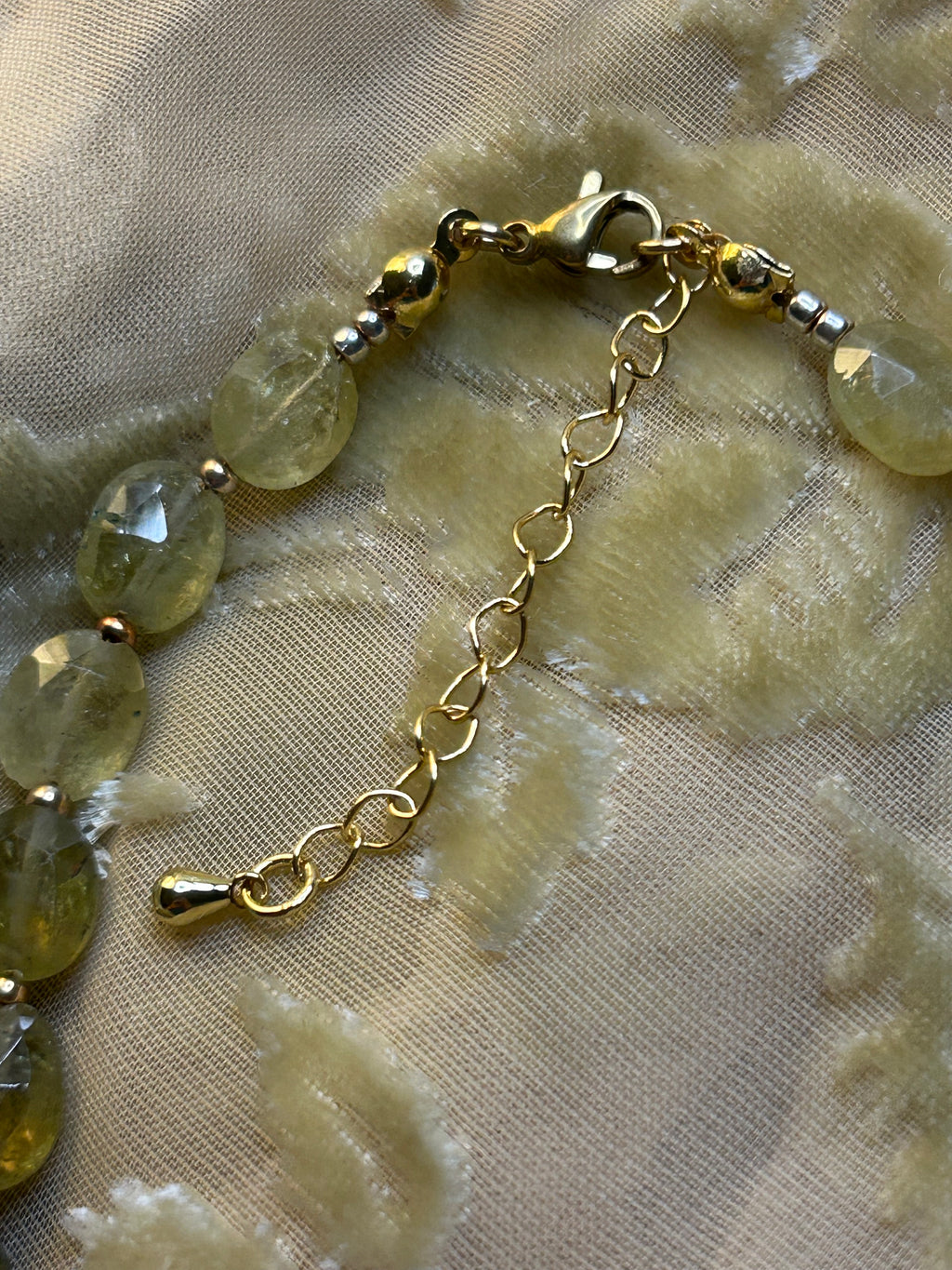 Gold bracelet with green beads on a textured beige fabric background