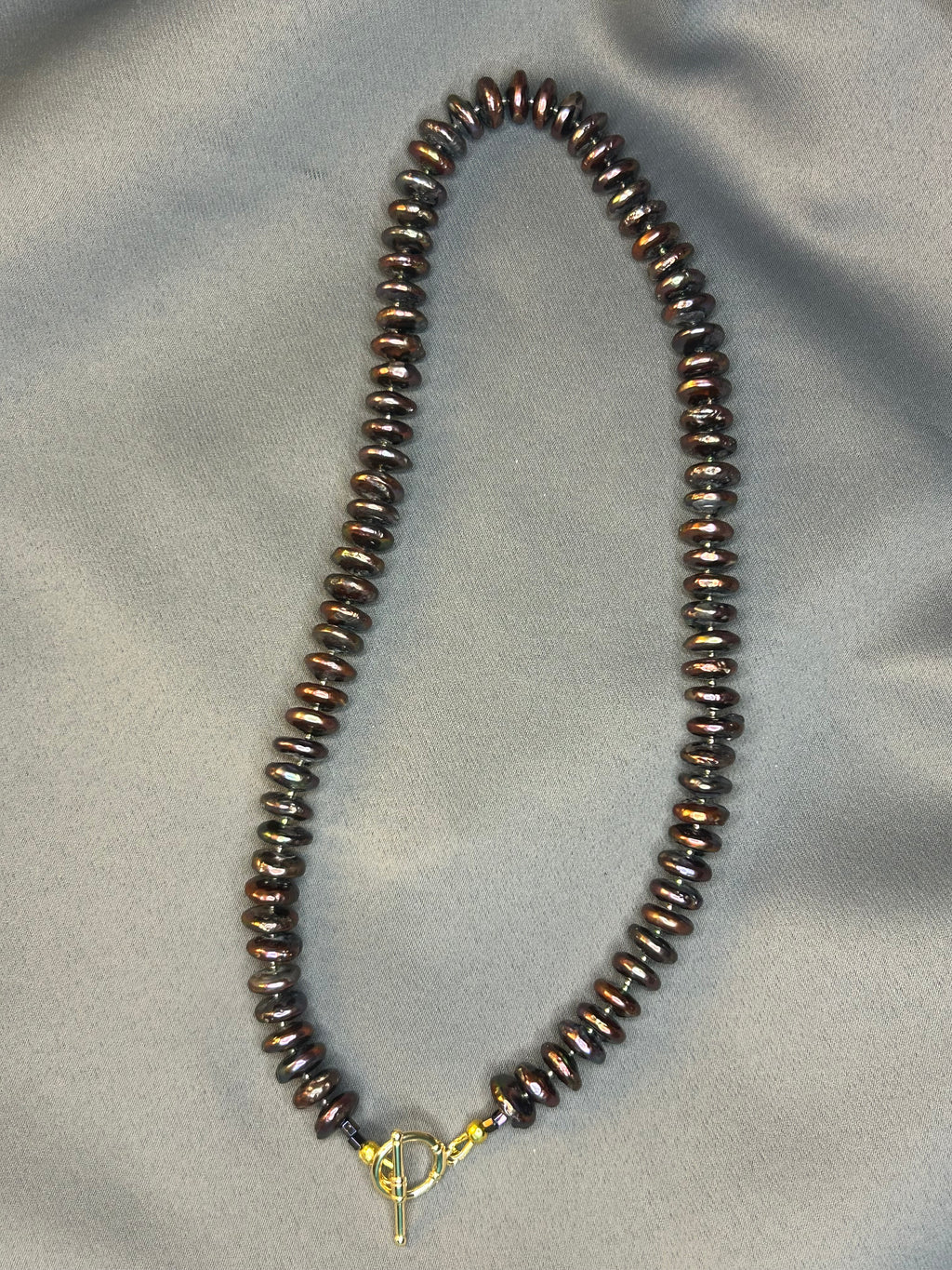 Beaded necklace with a gold clasp on a gray fabric background