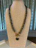 Necklace with gray beads and gold clasp on a beige display stand.