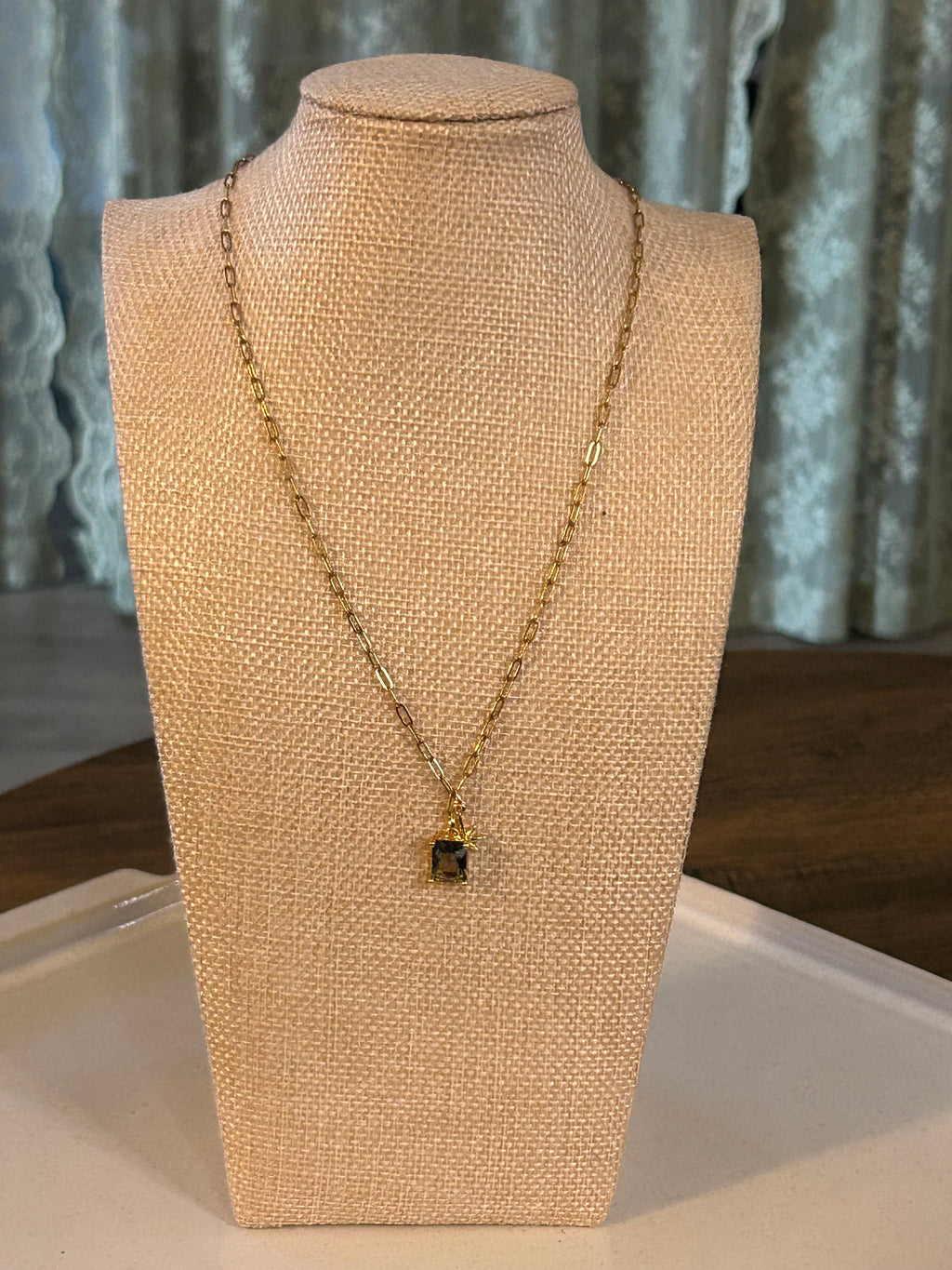 Gold necklace on a beige mannequin bust against a green background