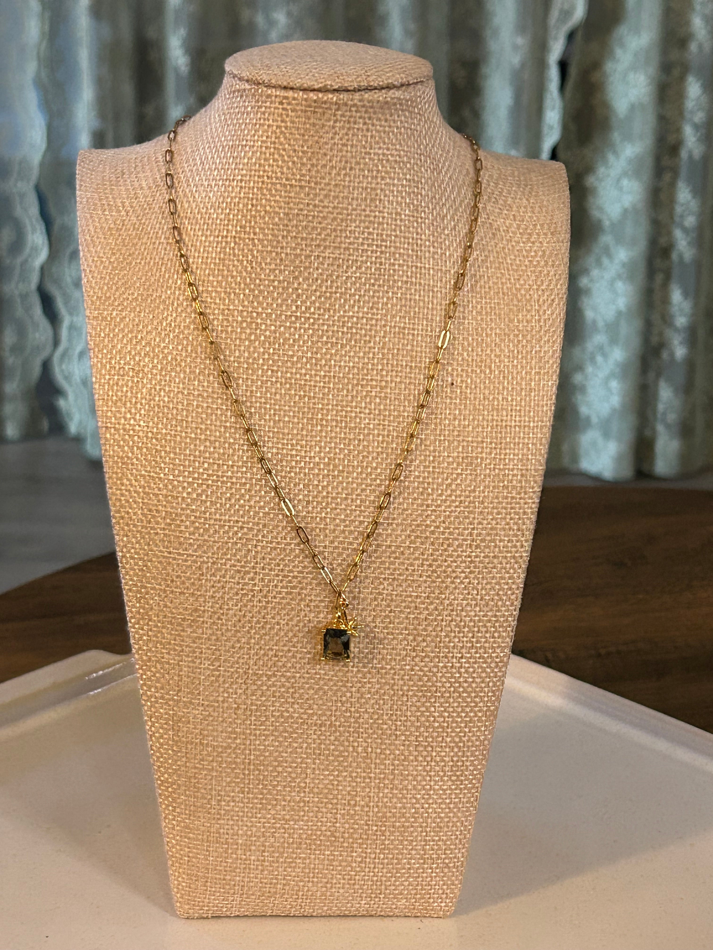 Gold necklace on a beige mannequin bust against a green background