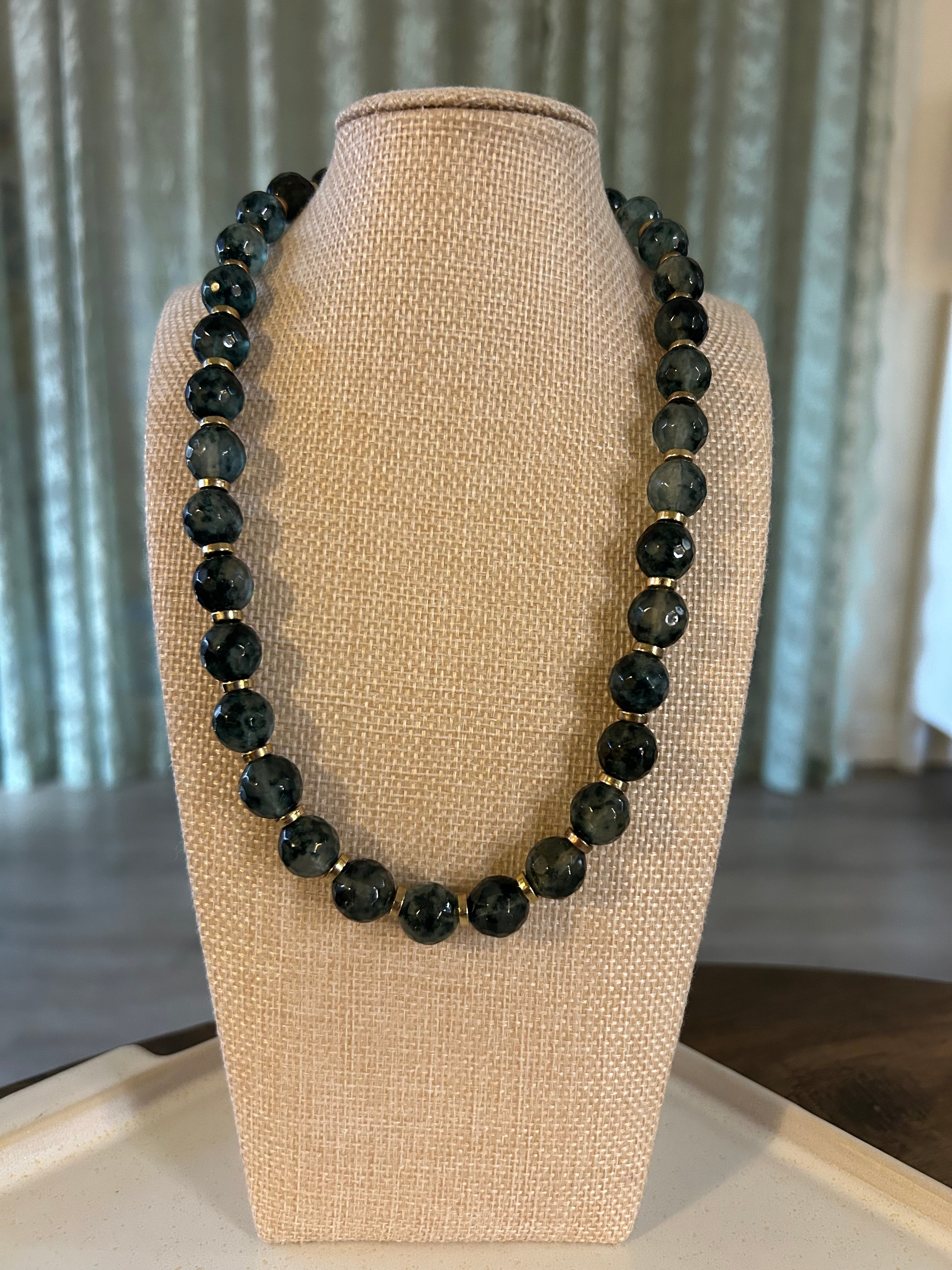 Green beaded necklace on a mannequin bust with a neutral background
