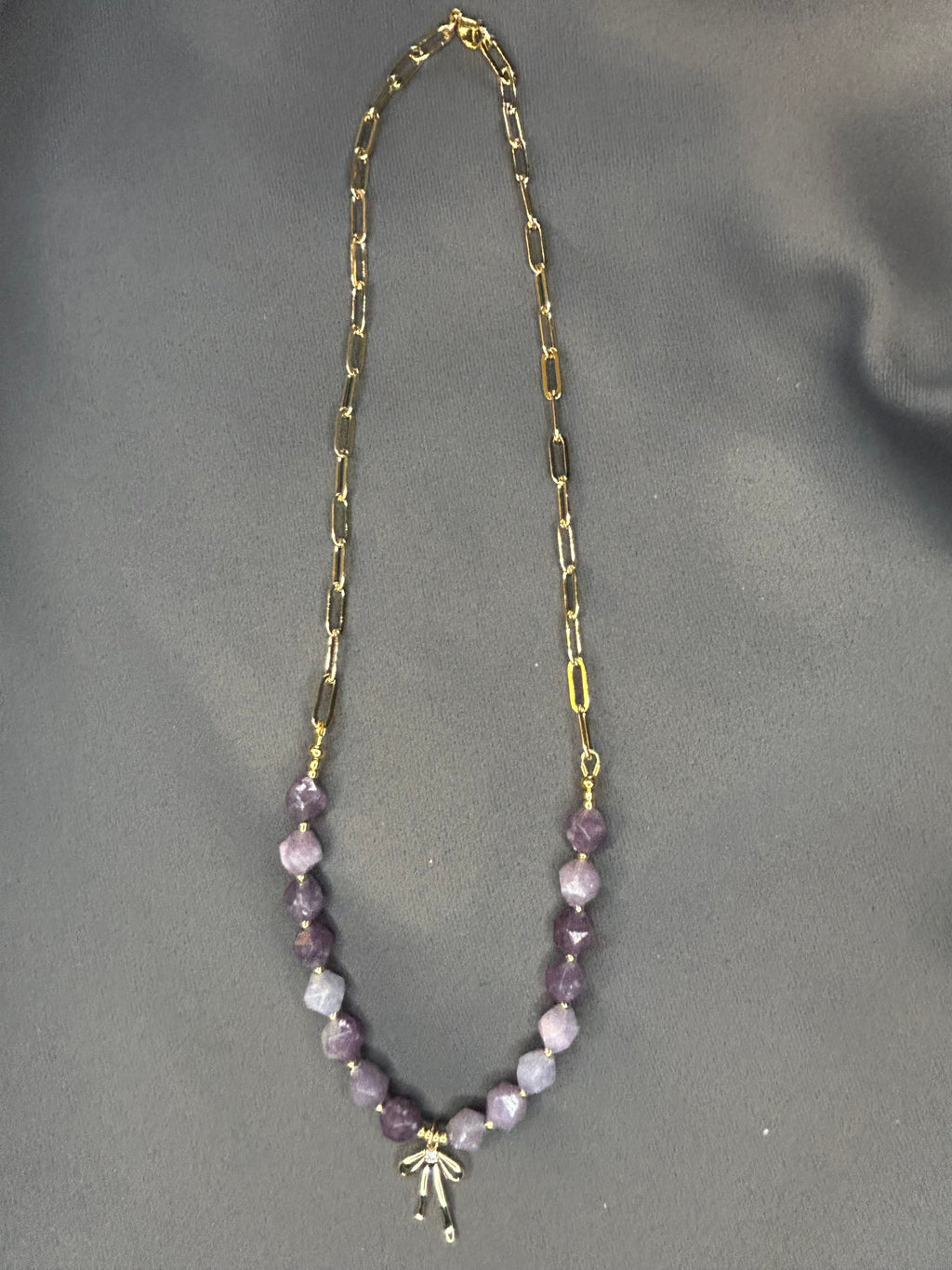 Necklace with gold chain and purple beads on a gray background