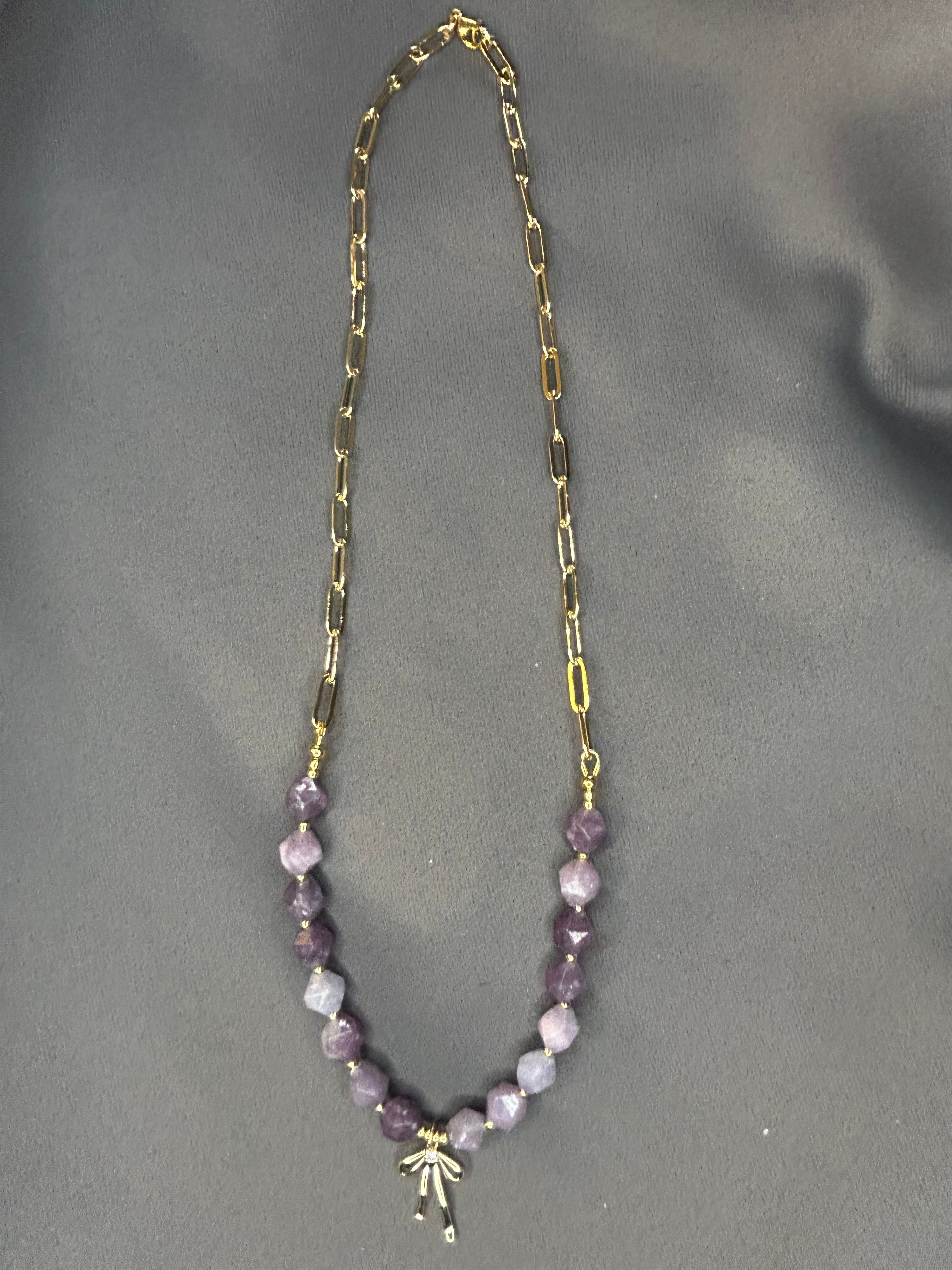 Necklace with gold chain and purple beads on a gray background
