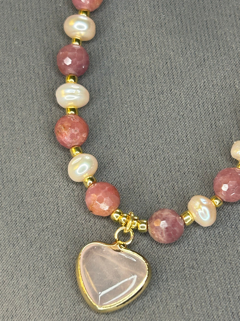 Necklace with pink and white beads and a heart-shaped charm on a gray background