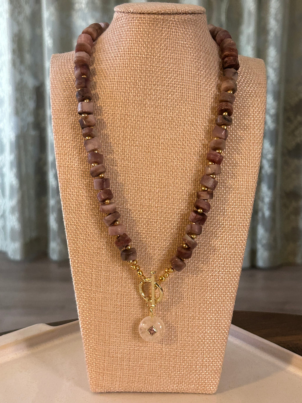 Dark-colored beaded necklace with a gold clasp on a beige display bust.