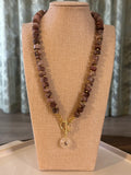 Dark-colored beaded necklace with a gold clasp on a beige display bust.