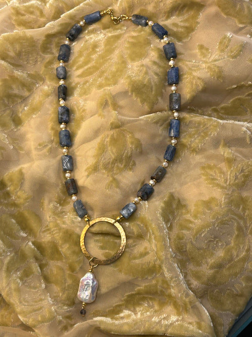 Necklace with blue beads and a gold ring on a textured fabric background