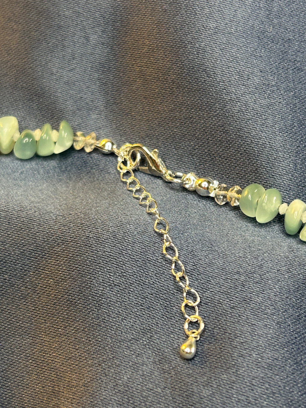 Necklace with green beads and silver chain on a gray fabric background