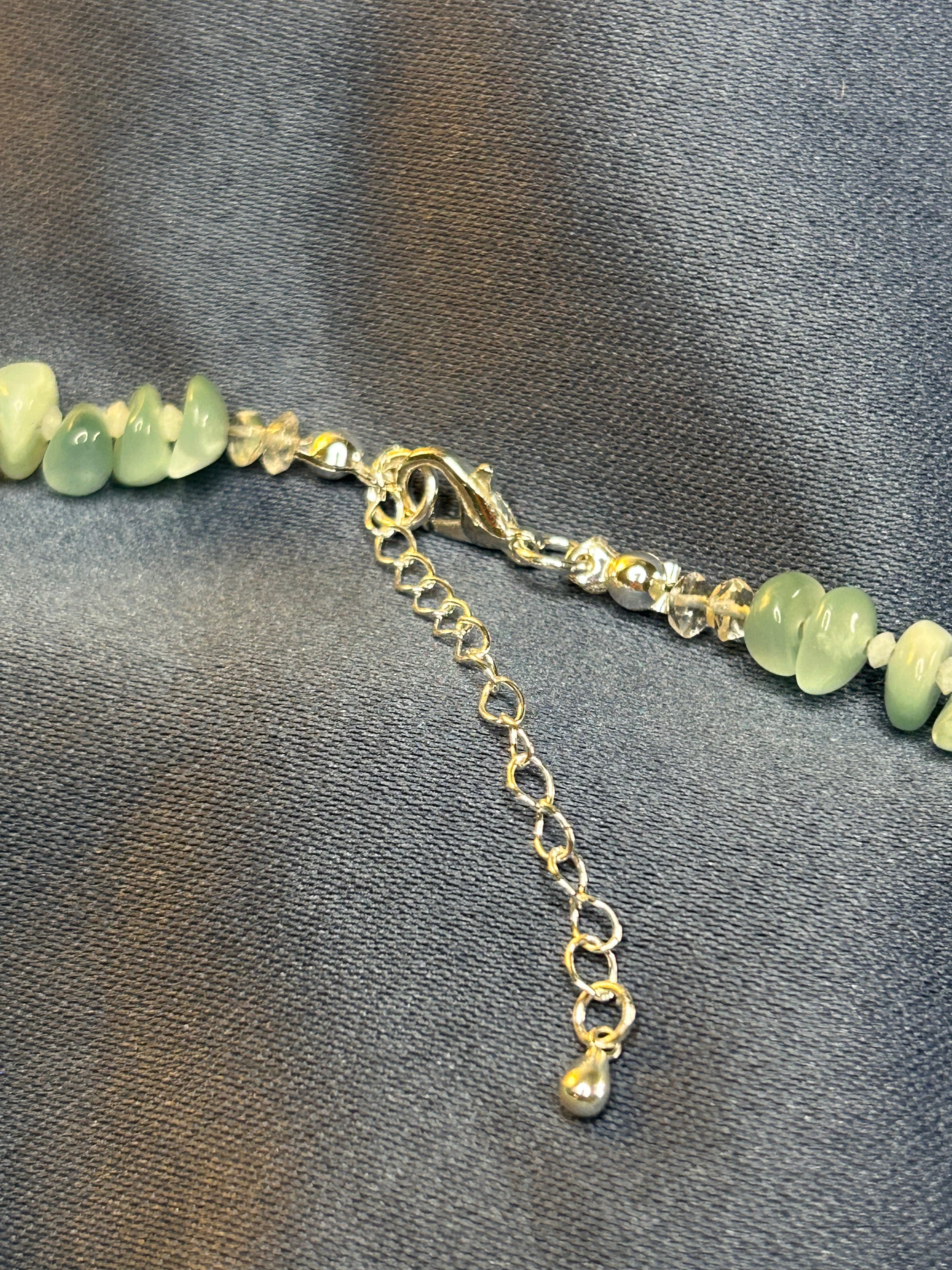 Necklace with green beads and silver chain on a gray fabric background
