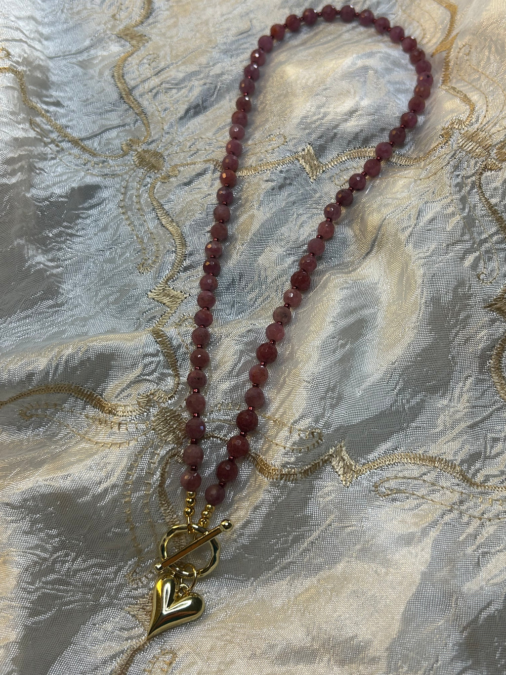 Necklace with red beads and a gold clasp on a textured fabric background