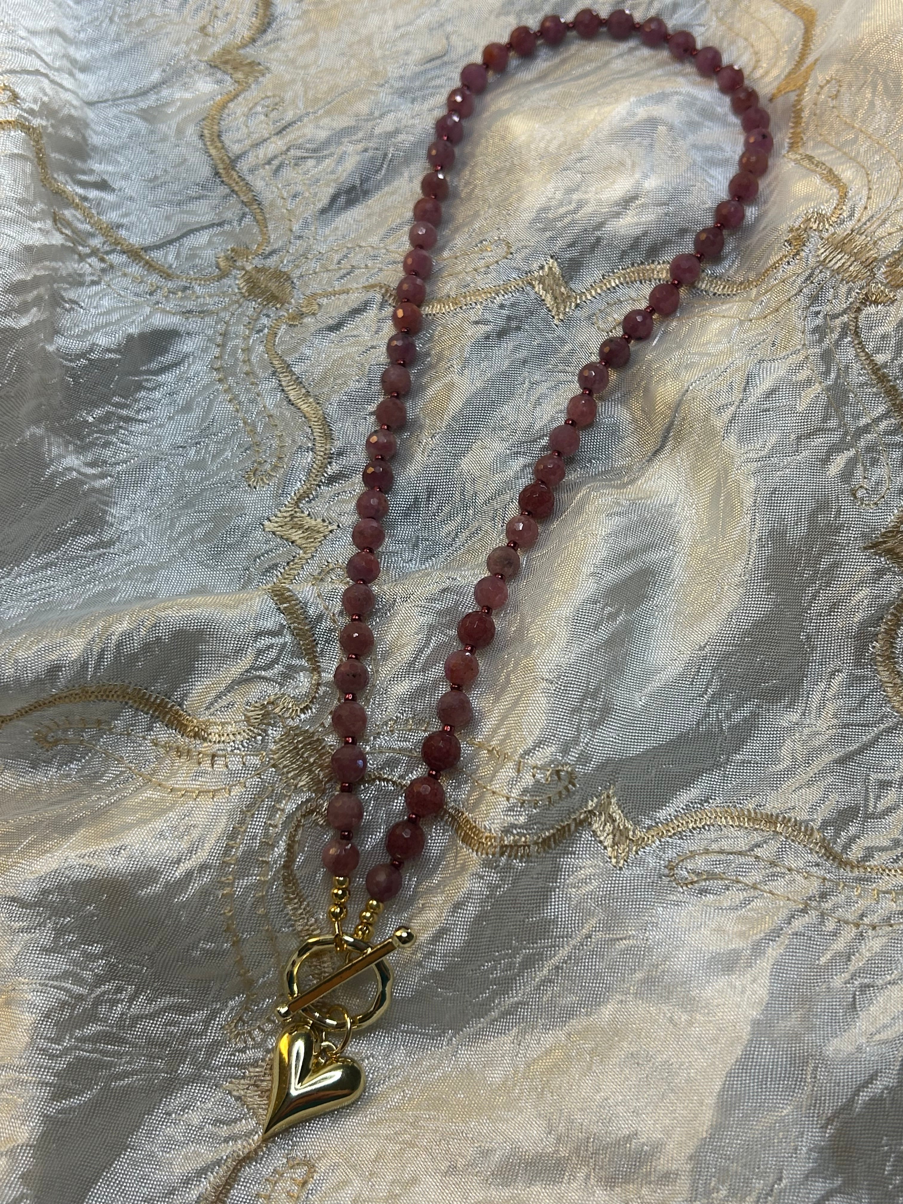 Necklace with red beads and a gold clasp on a textured fabric background
