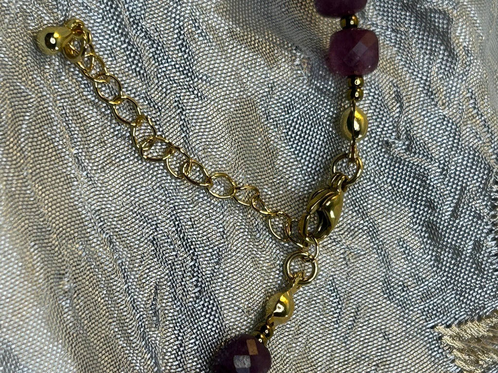 Gold chain with purple beads on a textured fabric background