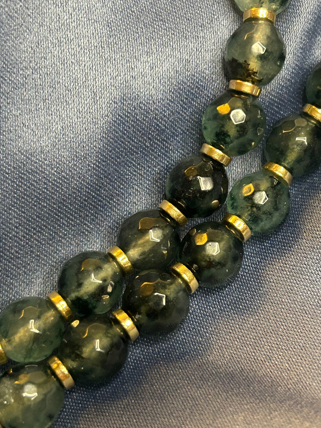 Close-up of green beaded necklace with gold accents on a textured fabric background
