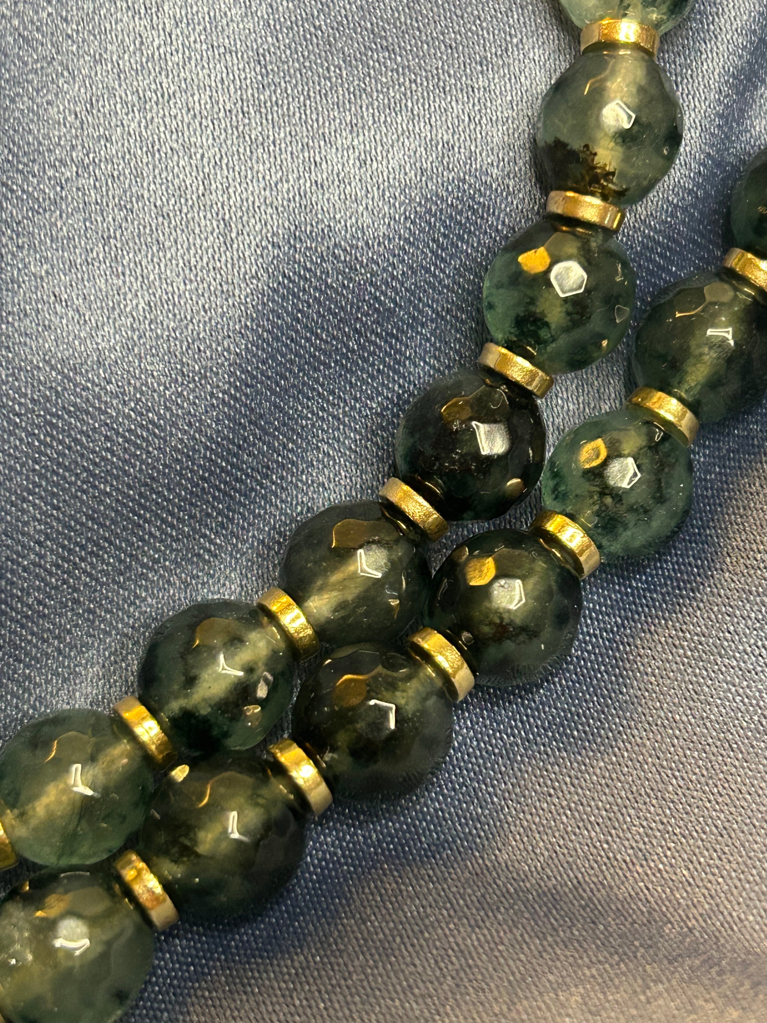 Close-up of green beaded necklace with gold accents on a textured fabric background
